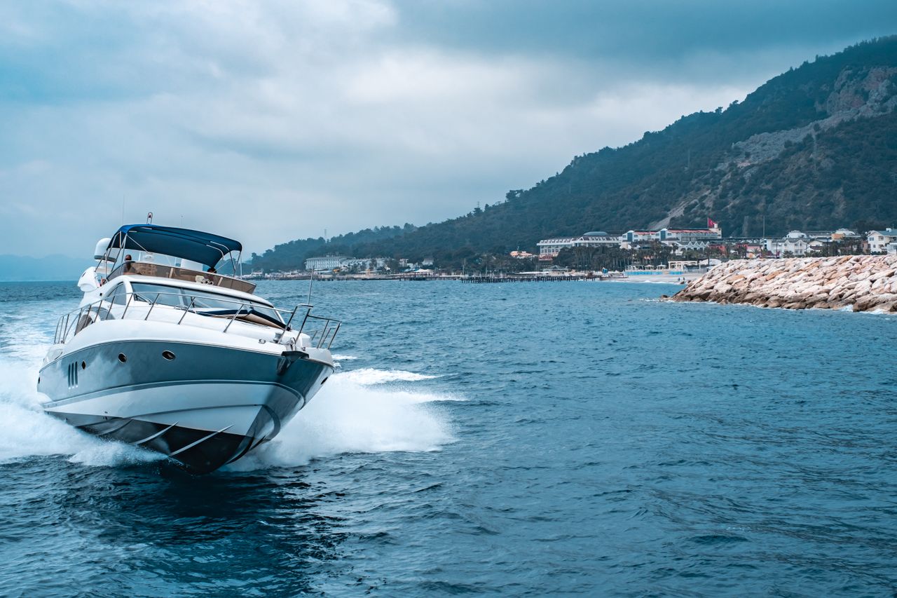 services-02 A luxury yacht glides through the blue waters off the coast of Antalya, Türkiye, with scenic mountains in the background.