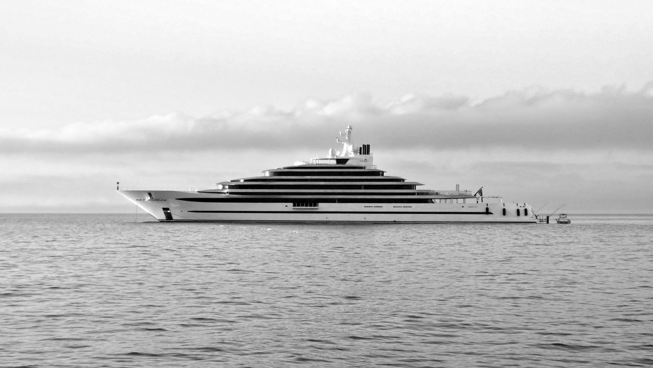 hero-img-02 A sleek yacht cruising the calm ocean under a cloudy sky in monochrome beauty.